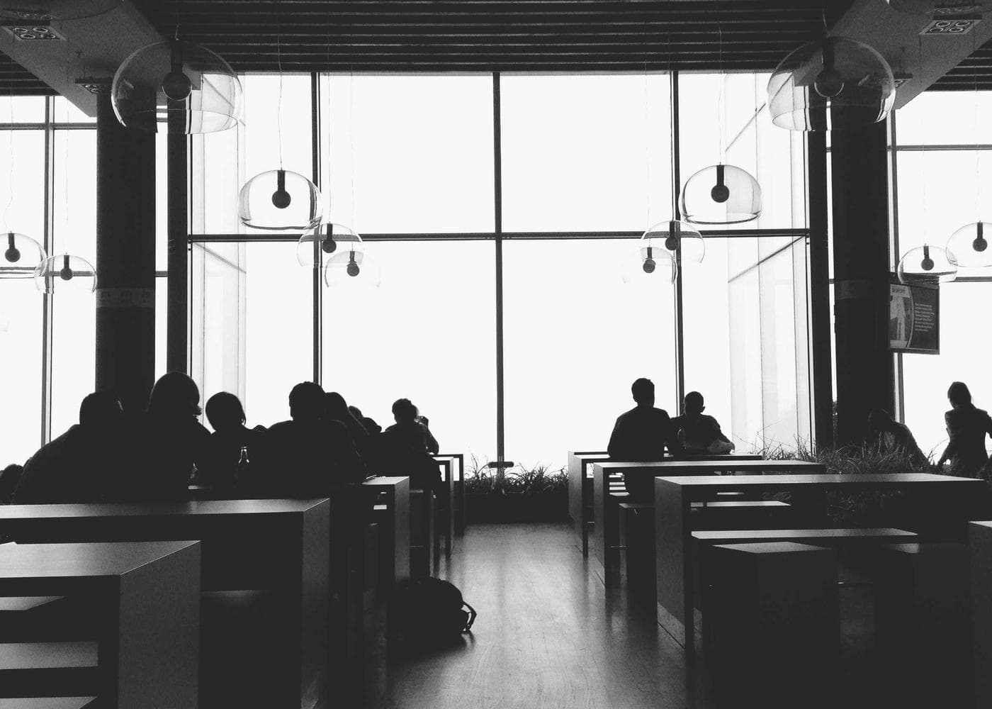 A bright room with tall windows and people seated in silhouette
