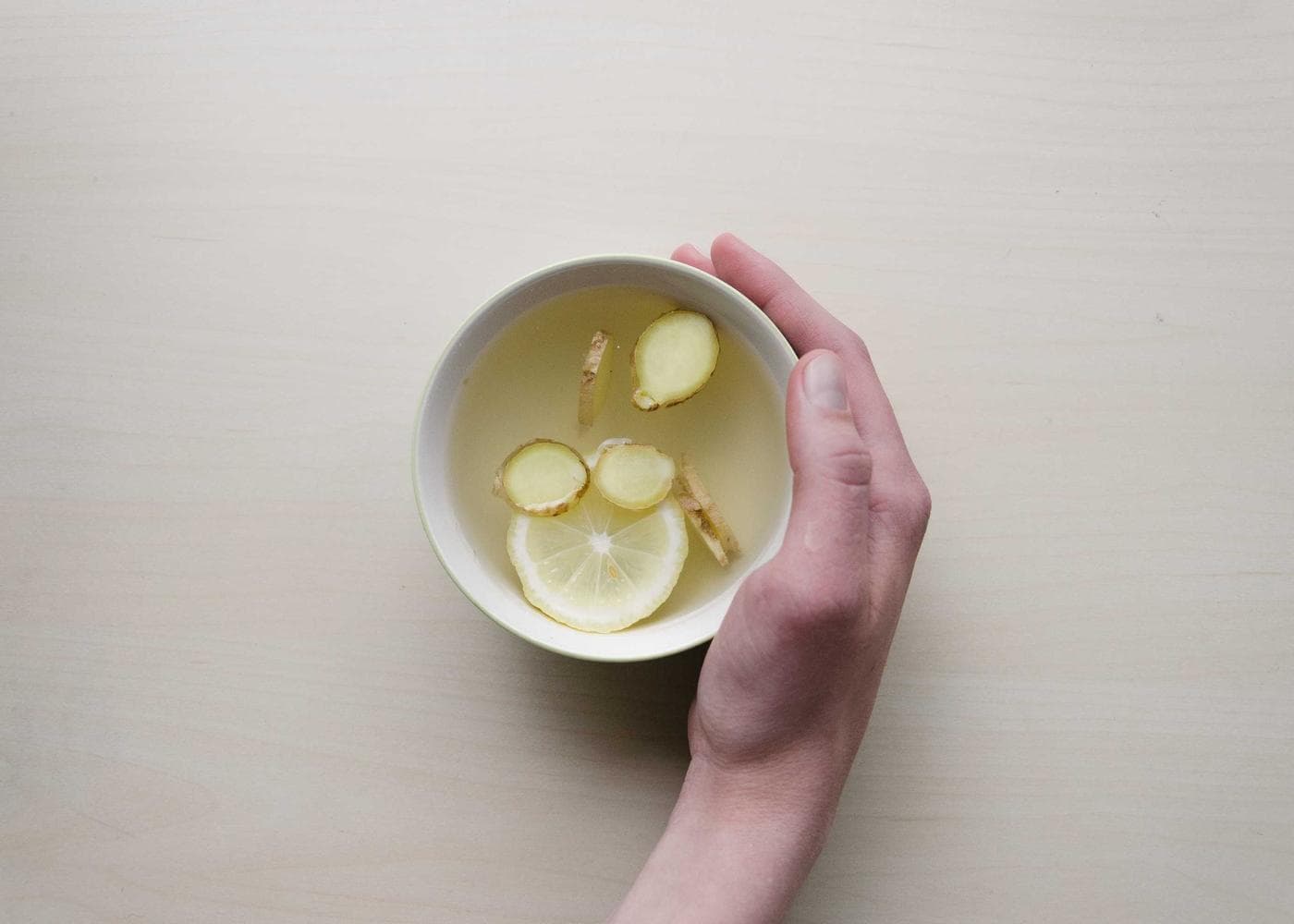 A hand holding a cup of hot water with lemon slices