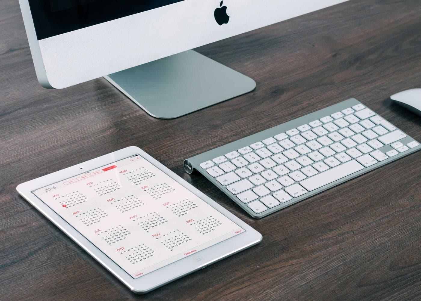 A desk with a monitor, keyboard and a tablet showing a calendar