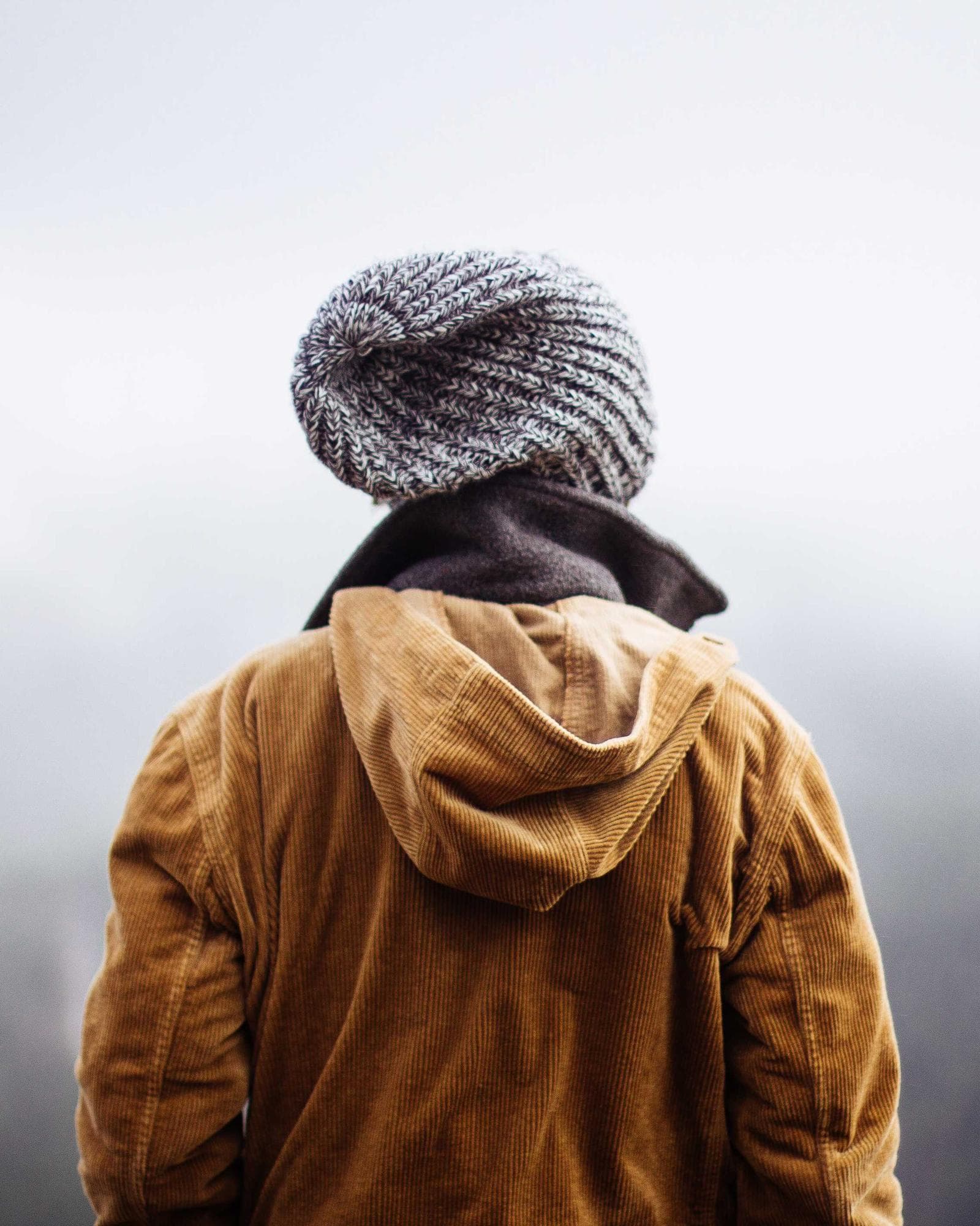 A person in a wool hat and ochre jacket looking out into morning fog