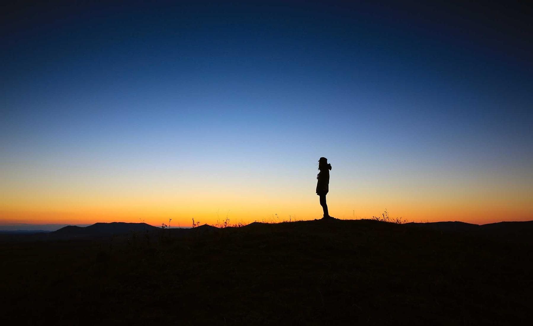 A figure on a shoreline under a dawn horizon