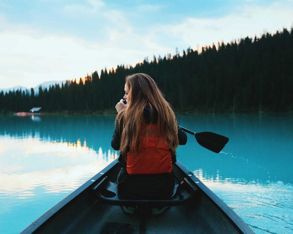 A paddler in a canoe on a calm lake lined with pine trees