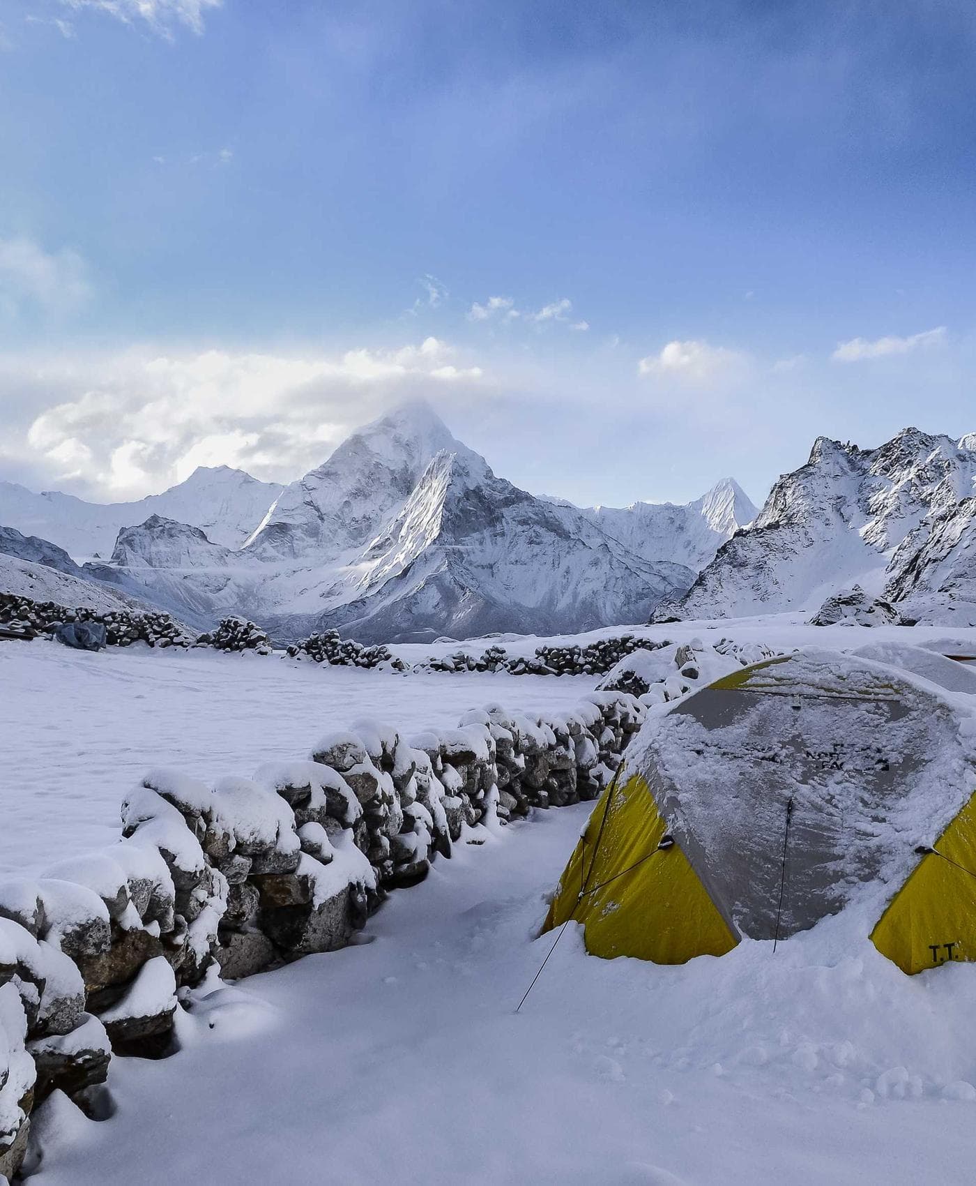 Two yellow tents pitched on a snowy ridge below alpine peaks