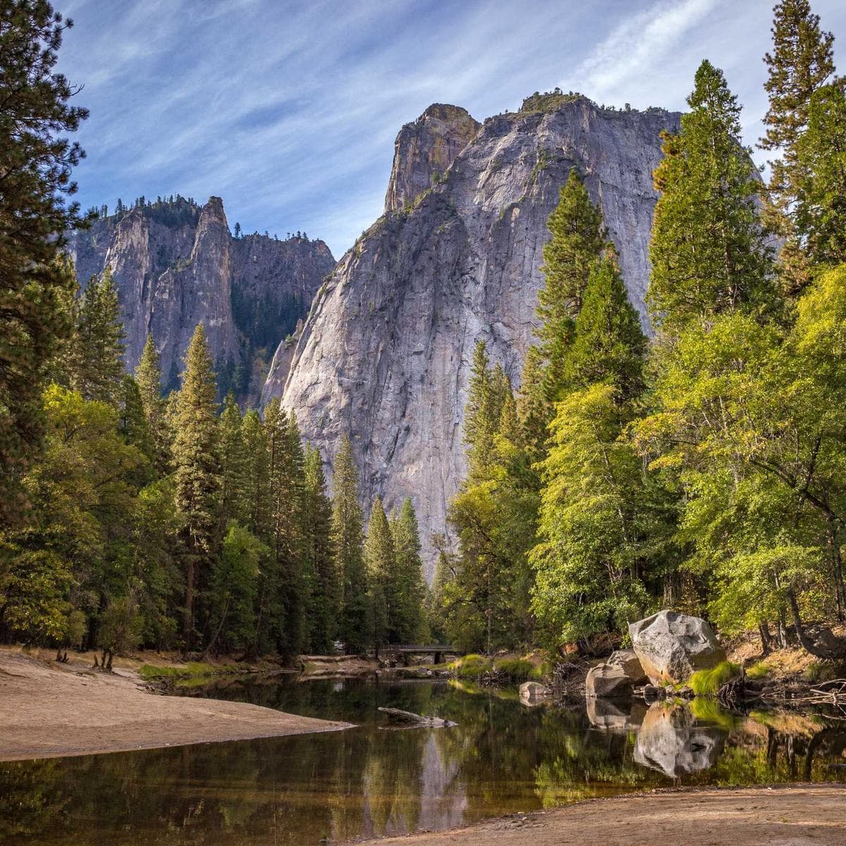 A campsite by a river in a forested valley below granite cliffs